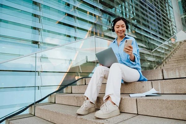 Asian Woman Headphones Using Gadgets While Sitting Stairs Outdoors — Stockfoto