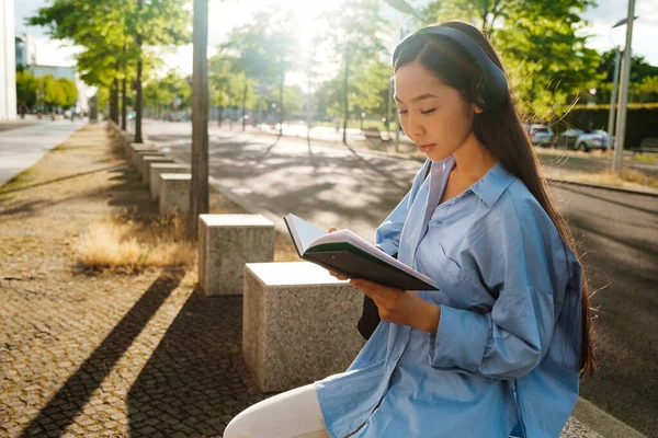 Asian Brunette Woman Headphones Reading Book While Sitting Bench Outdoors — Foto de Stock
