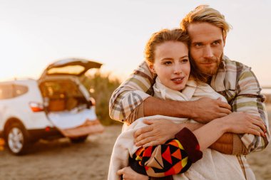 Happy young white couple hugging while walking by seashore on sunny day