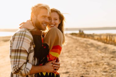 Happy young white couple hugging while walking by seashore on sunny day