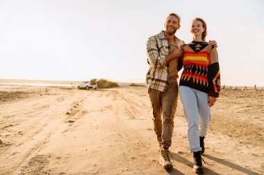 Happy young white couple hugging while walking by seashore on sunny day