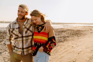 Happy young white couple hugging while walking by seashore on sunny day