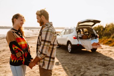 Happy young white couple smiling and holding hands while walking by seashore