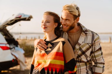 Happy young white couple smiling and hugging while walking by seashore