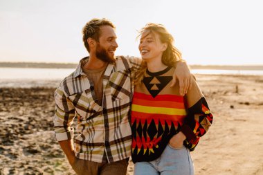 Happy young white couple smiling and hugging while walking by seashore