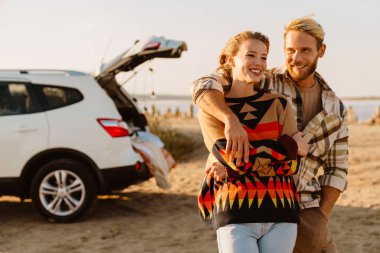 Happy young white couple smiling and hugging while walking by seashore