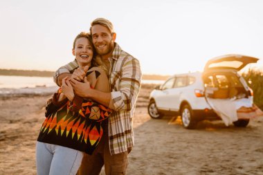 Happy young white couple smiling and hugging while walking by seashore