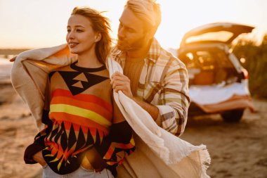 Happy young white couple smiling and hugging while walking by seashore