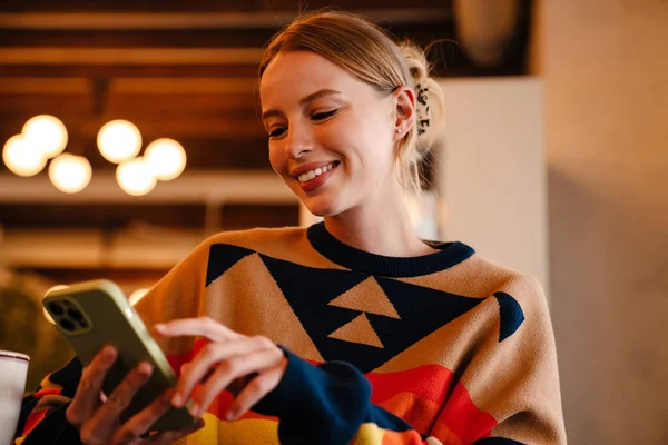Young White Woman Sweater Smiling Using Cellphone Cafe Indoors — Stockfoto