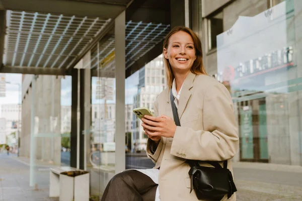 Young Beautiful Smiling Business Woman Holding Phone Looking Aside While — Stok fotoğraf