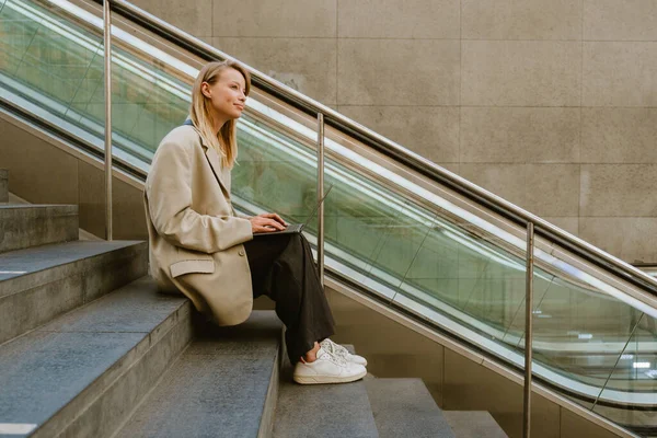 Genç Güzel Gülümseyen Bir Kadını Laptopuyla Merdivenlerde Otururken Yan Bakıyor — Stok fotoğraf