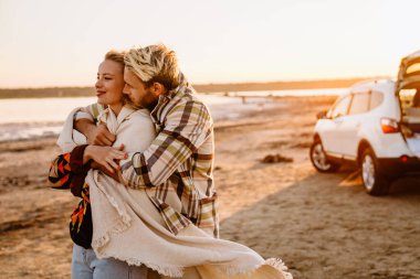 Happy young white couple smiling and hugging while walking by seashore