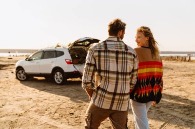 Happy young white couple smiling and looking at each other while walking by seashore