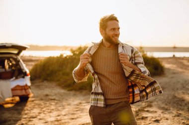 Happy young white man smiling while walking by seashore on sunny day