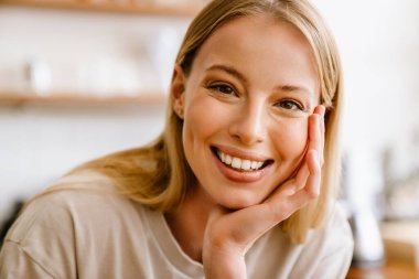Portrait of young beautiful attractive long-haired smiling woman propping her head and looking at camera