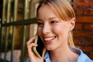Young white woman wearing shirt smiling and talking on cellphone outdoors