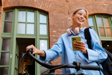 Young white woman using cellphone while standing by bicycle outdoors