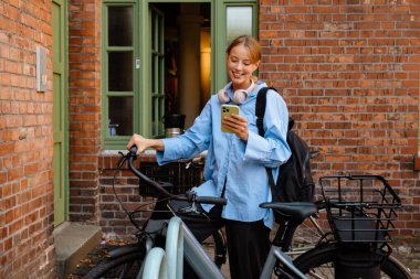 Young white woman using cellphone while standing by bicycle outdoors