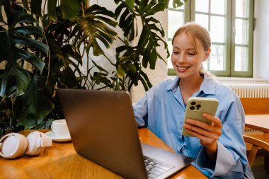 Young white businesswoman smiling and using laptop while sitting by table in cafe