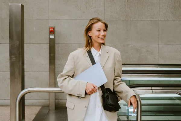 Mladá Bílá Žena Usmívá Drží Notebook Zatímco Stojí Eskalátoru Venku — Stock fotografie
