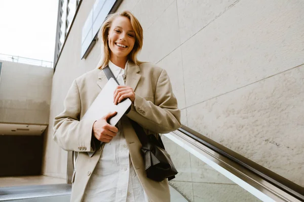 Young White Woman Smiling Holding Laptop While Standing Escalator Outdoors — Stockfoto