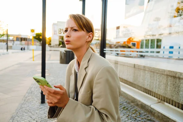 Young White Woman Frowning Using Cellphone While Sitting Bus Station — Stock Photo, Image