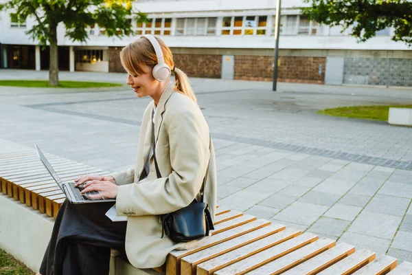 Young White Woman Using Laptop Headphones While Sitting Bench Outdoors — Zdjęcie stockowe