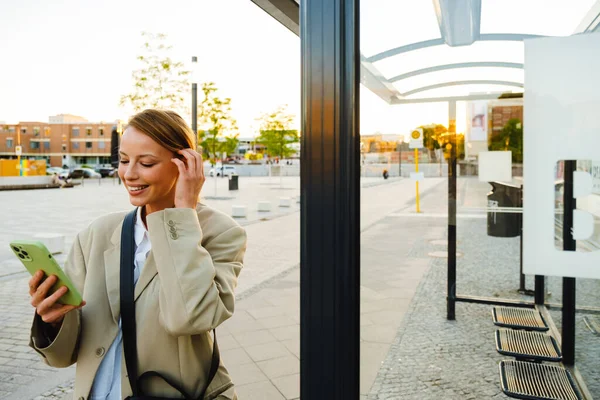 Young White Woman Smiling Using Cellphone While Standing Bus Station — Photo