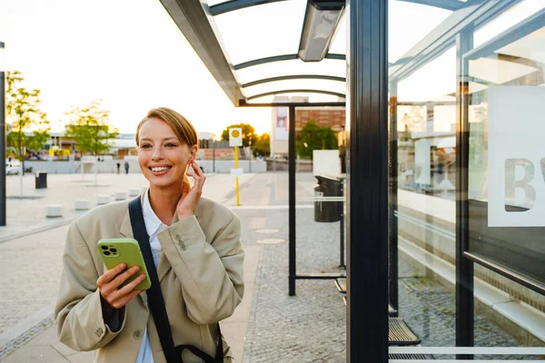 Young White Woman Smiling Using Cellphone While Standing Bus Station — Stok fotoğraf