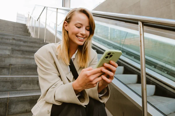 Genç Beyaz Kadın Merdivenlerde Otururken Gülümsüyor Cep Telefonu Kullanıyor — Stok fotoğraf