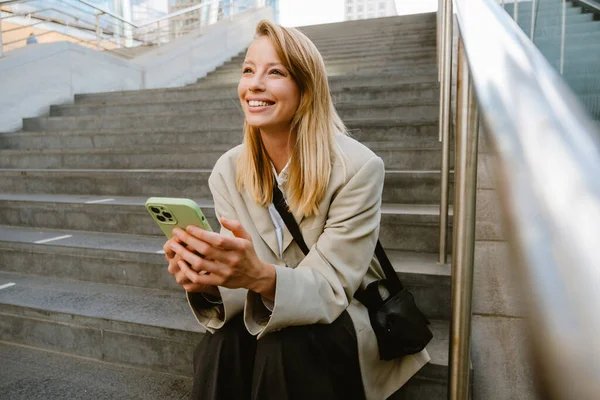 Joven Mujer Blanca Sonriendo Utilizando Teléfono Celular Mientras Está Sentado — Foto de Stock