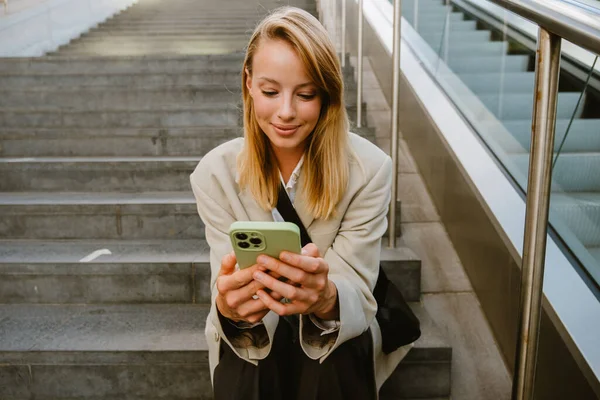Young White Woman Smiling Using Cellphone While Sitting Stairs Outdoors — Stok fotoğraf