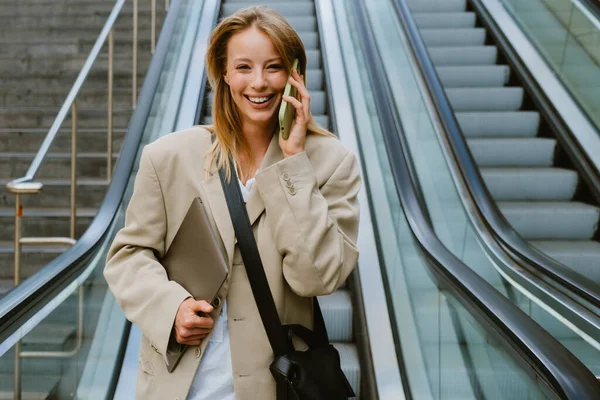 Young White Woman Talking Cellphone Holding Laptop While Going Escalator — Stockfoto