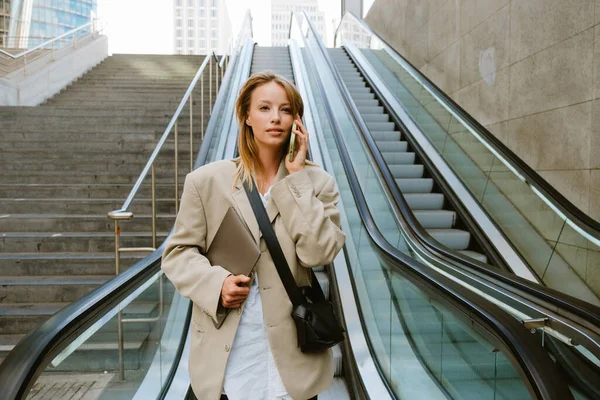 Young White Woman Talking Cellphone Holding Laptop While Going Escalator — Stok fotoğraf