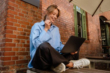 Ginger white woman in earphones working with laptop at cafe indoors
