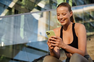 White young woman using mobile phone after yoga practice outdoors