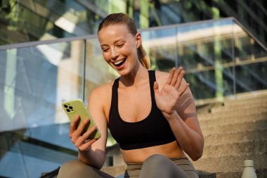 White young woman gesturing and using mobile phone after yoga practice outdoors