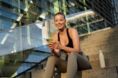 White young woman using mobile phone after yoga practice outdoors