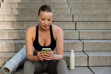 White young woman using mobile phone after yoga practice outdoors