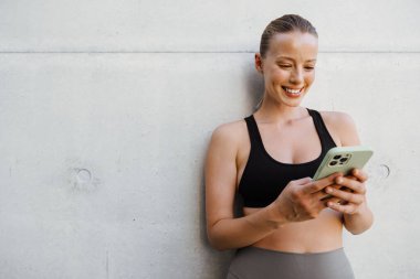 White young woman using mobile phone after yoga practice outdoors