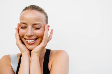 White young woman in sportswear smiling at camera while posing by wall outdoors