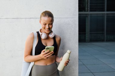 White young woman using mobile phone after yoga practice outdoors