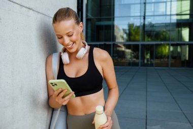 White young woman using mobile phone after yoga practice outdoors
