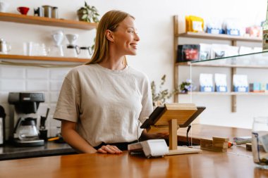 Blonde white barista woman working with tablet computer in cafe indoors