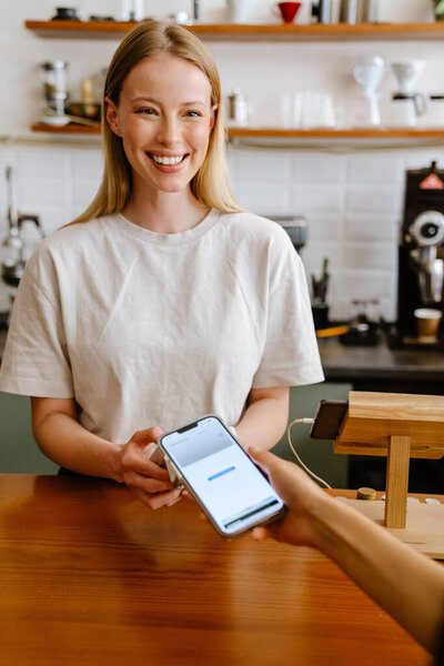 Blonde white barista woman working with terminal in cafe indoors