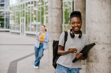 Young black woman smiling and using cellphone while standing at city street