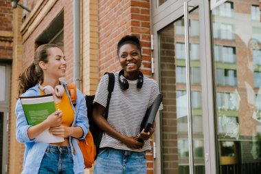 Young multinational girls with exercise books smiling and walking together outdoors
