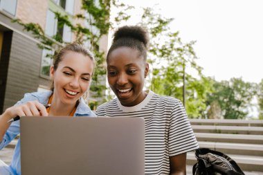 Young multiracial women doing homework with laptop while sitting on stairs outdoors