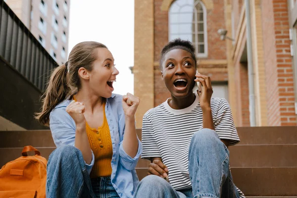 Excited Multinational Girls Screaming Using Cellphone Together While Sitting Stairs — Stok fotoğraf