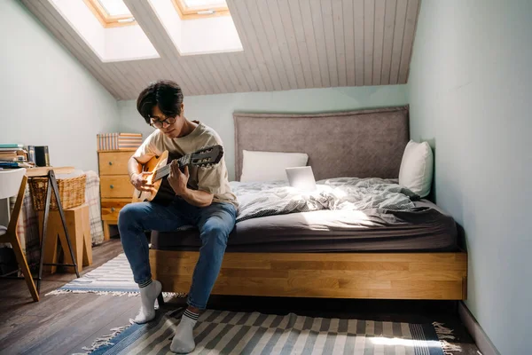Jovem Asiático Homem Fones Ouvido Tocando Guitarra Enquanto Sentado Cama — Fotografia de Stock